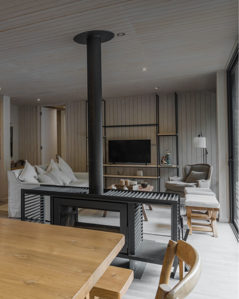 Un acogedor salón con una estufa de leña como punto focal, que refleja el diseño moderno y funcional de una vivienda modular. La combinación de muebles cómodos y una decoración elegante crea un ambiente ideal para el descanso. Esta casa prefabricada es perfecta como segunda vivienda. Tecno Fast Home.
