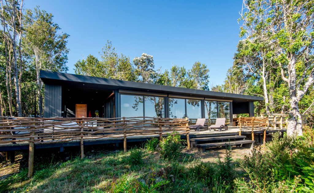 Casa modular con amplios ventanales y un deck de madera, rodeada de naturaleza, ideal como segunda vivienda. Diseño moderno y funcional, perfecta para disfrutar del aire libre. Tecno Fast Home.
