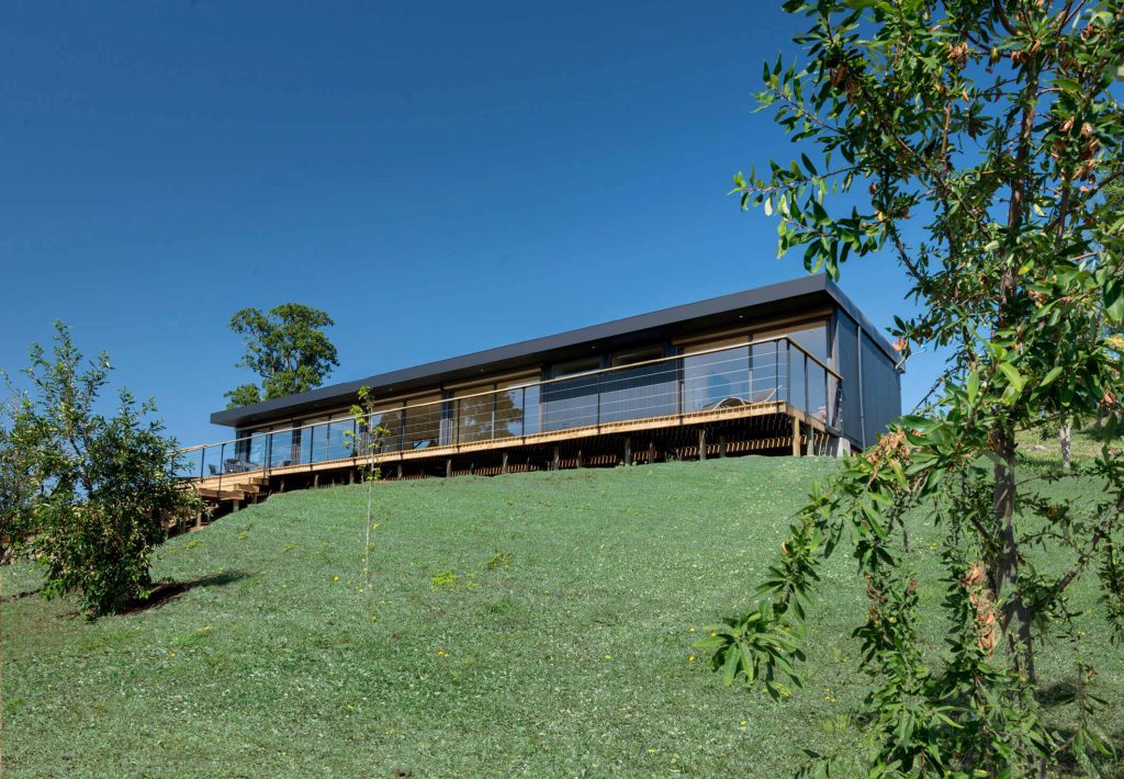 Casa modular situada en un entorno natural, con un diseño moderno y amplio balcón que ofrece vistas panorámicas. Ideal como vivienda permanente o segunda vivienda. Marca: Tecno Fast Home.