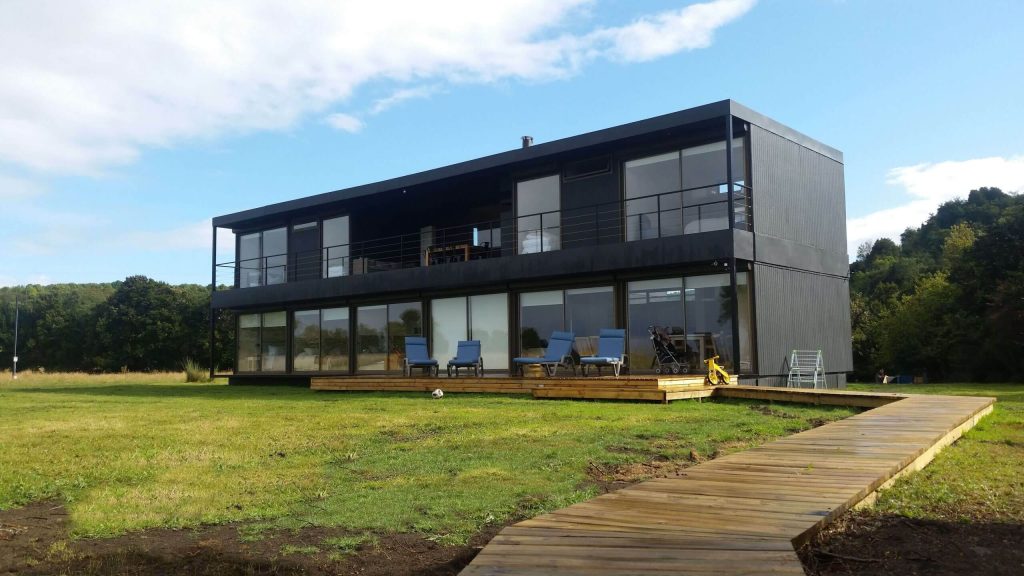 Casa modular de diseño contemporáneo con amplios ventanales y terraza de madera, ideal para una vivienda secundaria o un proyecto de vivienda modular. Su estilo moderno y funcional se adapta perfectamente a diferentes entornos. Tecno Fast Home.