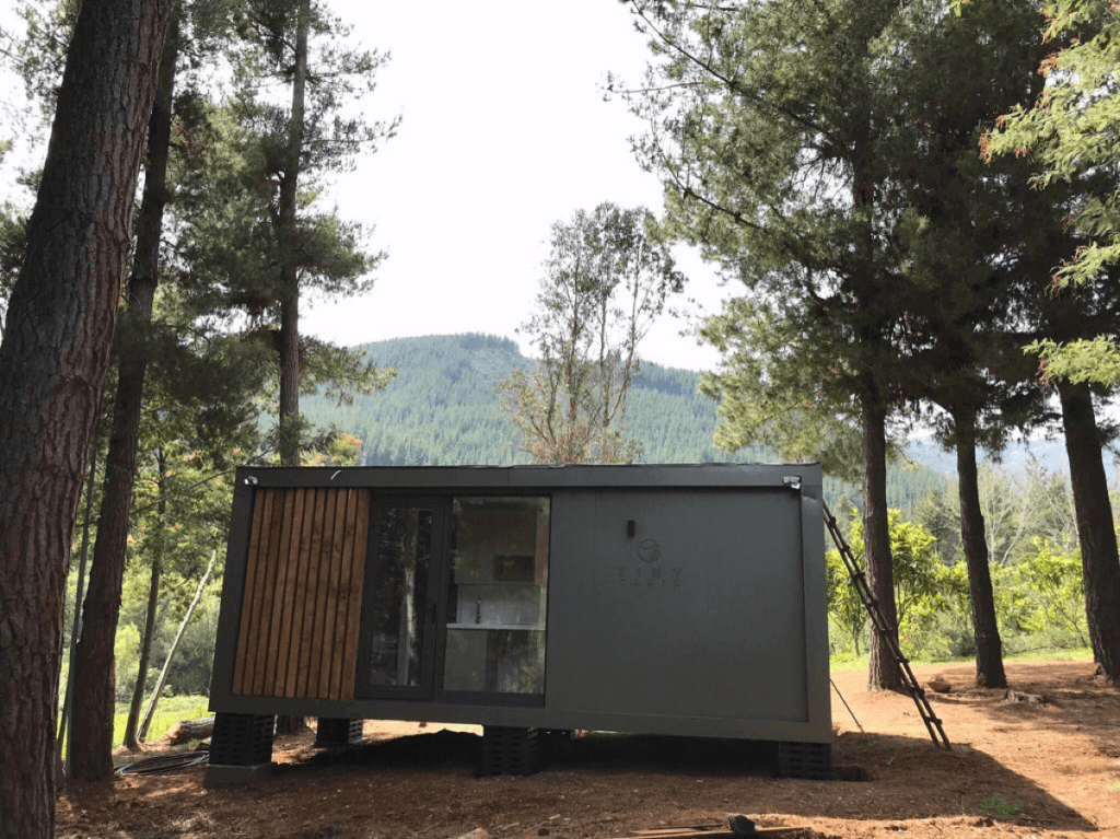 Casa modular ubicada en un entorno natural, rodeada de árboles y montañas, ideal como segunda vivienda o refugio. Diseño moderno y funcional que se integra con el paisaje. Tecno Fast Home.