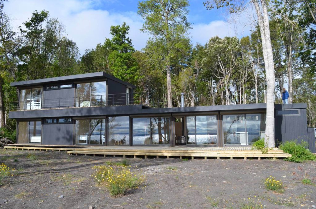 Casa modular moderna con amplios ventanales y diseño contemporáneo, ubicada en un entorno natural. Ideal como vivienda prefabricada o segunda vivienda. Destacada por su funcionalidad y estética, esta construcción representa una opción versátil para quienes buscan comodidad y estilo. Tecno Fast Home.