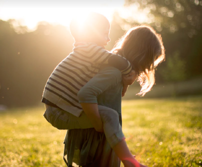 Una madre lleva a su hijo a caballito en un entorno natural iluminado por el sol, simbolizando la calidez y la cercanía familiar que se puede disfrutar en una casa modular de vacaciones. Tecno Fast Home.