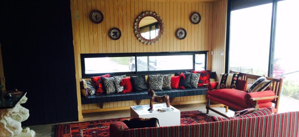 Espacio interior acogedor de una vivienda modular, con un diseño contemporáneo que incluye un sofá con cojines coloridos y una mesa central, ideal para disfrutar en familia. La iluminación natural resalta la calidez de la madera en las paredes, creando un ambiente agradable para una segunda vivienda. Tecno Fast Home.