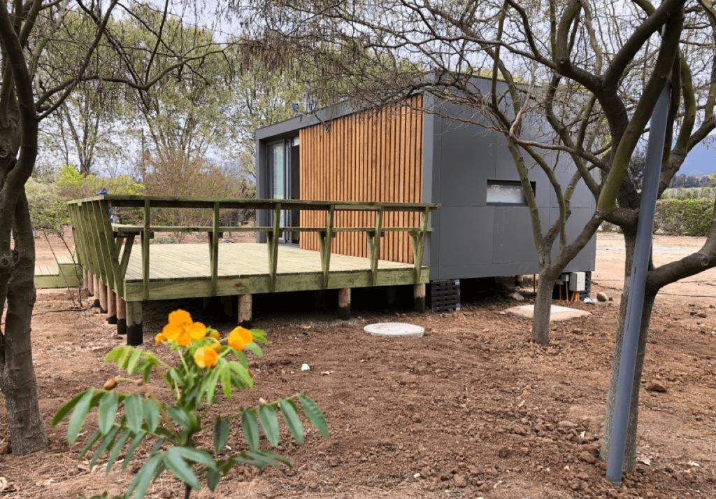 Casa modular con diseño contemporáneo, ubicada en un entorno natural, ideal como segunda vivienda. Presenta una estructura de madera y un deck que se integra con el paisaje. Perfecta para disfrutar de la tranquilidad. Marca: Tecno Fast Home.