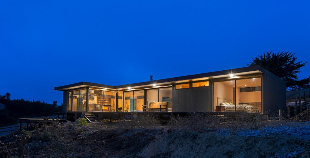 Casa modular iluminada en la noche, con un diseño moderno y amplio espacio exterior, ideal como vivienda secundaria o casa prefabricada. La estructura resalta por su funcionalidad y estilo contemporáneo. Tecno Fast Home.