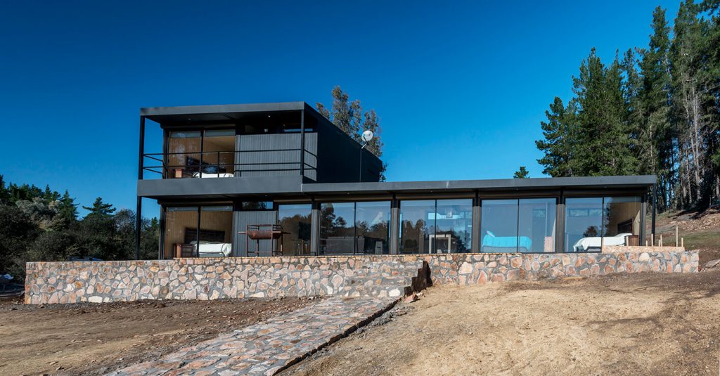 Casa moderna de diseño contemporáneo con amplios ventanales y estructura de acero, situada en un entorno natural. Ideal como vivienda modular o segunda residencia. Marca Tecno Fast Home.