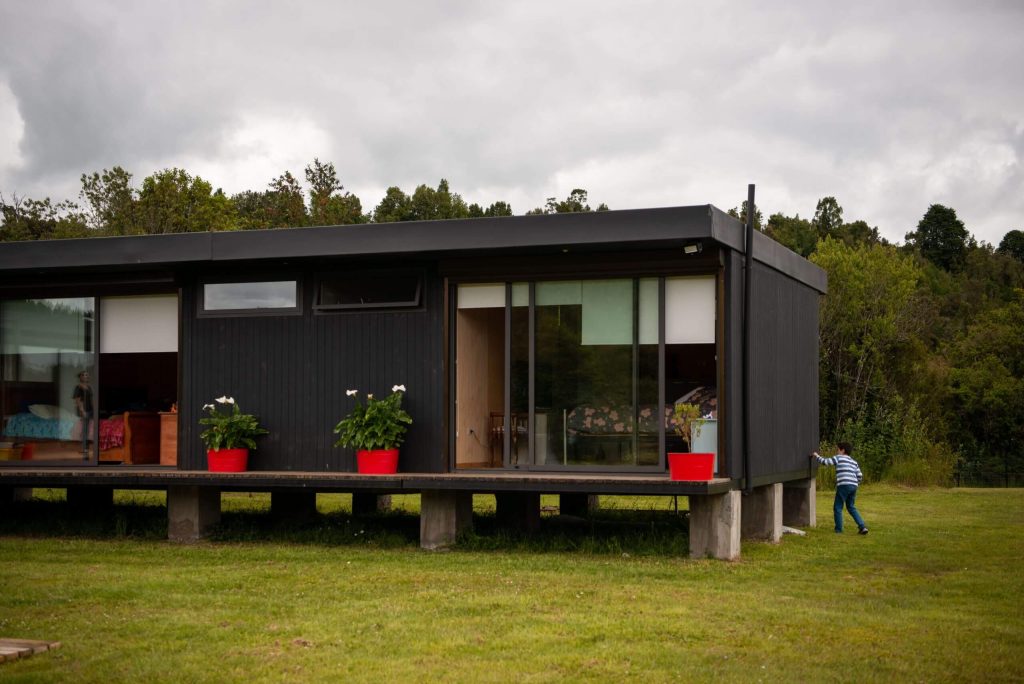 Casa modular moderna con diseño contemporáneo, ubicada en un entorno natural. Su estructura incluye amplios ventanales y un porche, ideal para disfrutar del aire libre. Perfecta como segunda vivienda o vivienda prefabricada. Tecno Fast Home.