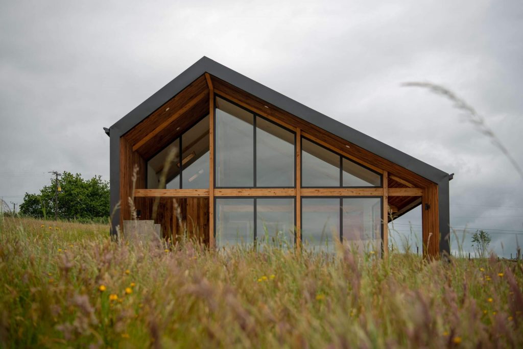 Casa modular con amplios ventanales y diseño moderno, situada en un entorno natural, ideal como segunda vivienda o espacio vacacional. Esta vivienda prefabricada combina estética y funcionalidad, destacando su estructura en madera. Tecno Fast Home.