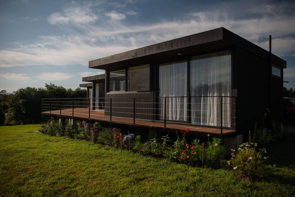 Casa modular contemporánea con amplios ventanales y terraza, ideal como segunda vivienda o vivienda prefabricada. Diseño moderno que se integra con el entorno natural. Tecno Fast Home.