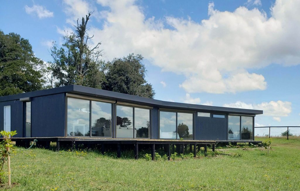 Casa modular de diseño contemporáneo, con grandes ventanales y estructura elevada, ideal para una segunda vivienda en un entorno natural. Este modelo representa una opción de vivienda prefabricada que combina estética y funcionalidad. Tecno Fast Home.
