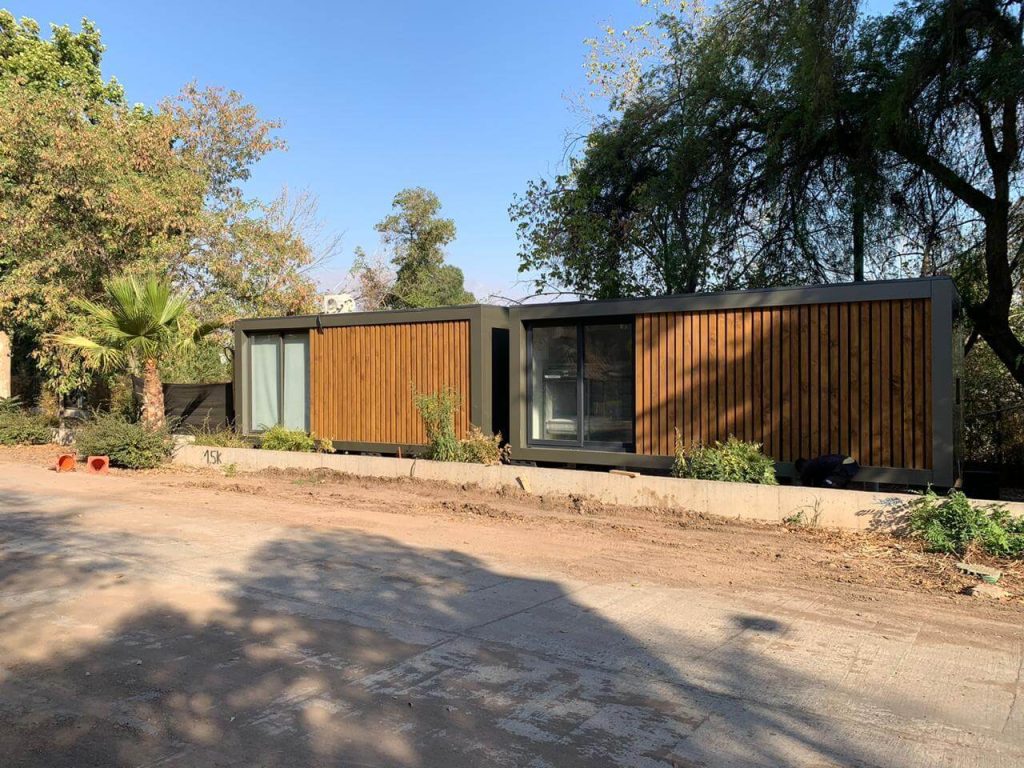 Casa modular de diseño contemporáneo con revestimiento de madera y grandes ventanales, ideal como vivienda secundaria. Espacio exterior rodeado de vegetación, perfecta para disfrutar de la naturaleza. Marca Tecno Fast Home.