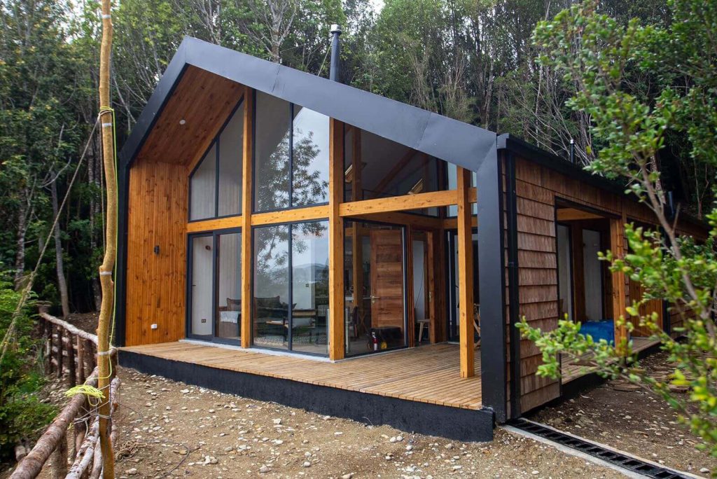 Casa modular con diseño contemporáneo, destacando su estructura de madera y amplios ventanales que permiten la entrada de luz natural. Ideal como vivienda secundaria o para quienes buscan una alternativa de vivienda eficiente. Marca Tecno Fast Home.