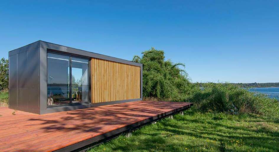 Casa modular con diseño contemporáneo, rodeada de naturaleza y con una amplia terraza de madera. Ideal como vivienda secundaria o casa prefabricada. Marca Tecno Fast Home.