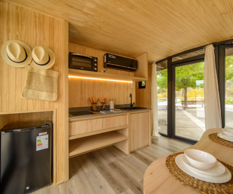 Interior de una casa modular con diseño contemporáneo, donde se aprecian acabados en madera, cocina equipada y amplios ventanales que permiten la entrada de luz natural. Ideal como segunda vivienda o vivienda prefabricada. Marca Tecno Fast Home.