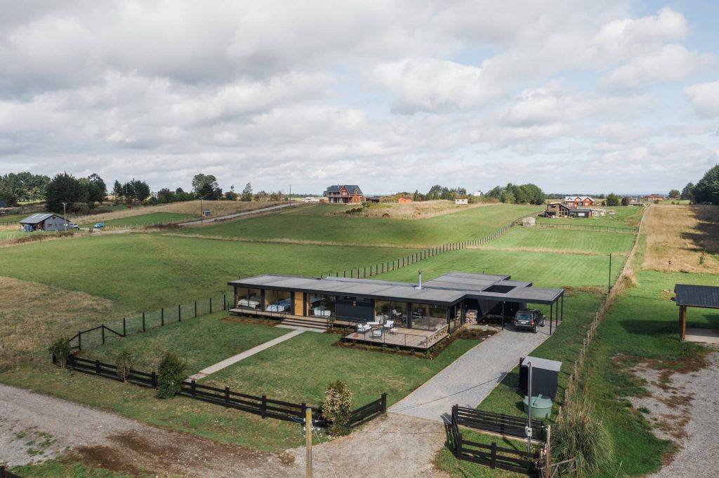 Una vista panorámica de una casa modular ubicada en un amplio terreno verde, ideal como segunda vivienda. La construcción destaca por su diseño moderno y funcional, rodeada de un entorno natural. Este tipo de vivienda prefabricada ofrece comodidad y estilo. Tecno Fast Home.