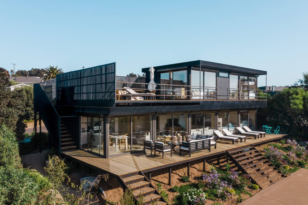 Casa modular contemporánea con amplios ventanales, rodeada de un hermoso jardín con flores. Ideal como vivienda secundaria o casa prefabricada para disfrutar de la naturaleza. Tecno Fast Home.