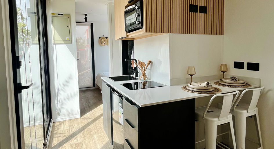 Una cocina moderna y funcional dentro de una vivienda modular, equipada con electrodomésticos de última generación y un diseño minimalista. Los tonos claros y oscuros contrastan, creando un espacio acogedor para disfrutar. Esta casa prefabricada es ideal como segunda vivienda. Tecno Fast Home.
