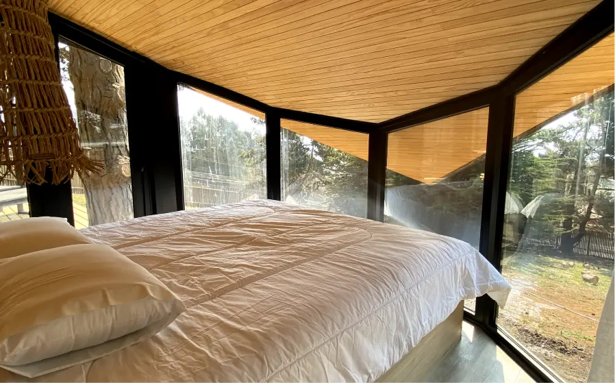 Una acogedora habitación con grandes ventanales que permiten disfrutar de la vista exterior, ideal para una vivienda modular. La iluminación natural resalta el diseño contemporáneo y funcional de esta casa prefabricada. Un espacio perfecto para relajarse y conectar con la naturaleza, ideal como segunda vivienda. Tecno Fast Home.
Un dormitorio moderno con un diseño innovador, caracterizado por su estructura de vidrio que proporciona una sensación de amplitud. Este tipo de casa modular es ideal para quienes buscan una vivienda eficiente y