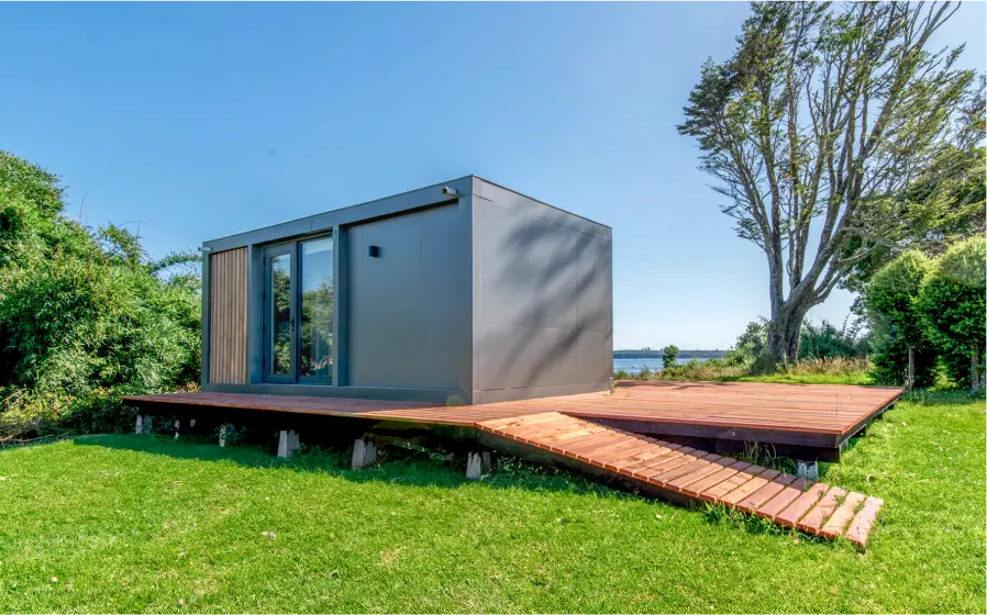 Casa modular con diseño contemporáneo, ubicada en un entorno natural, rodeada de césped y árboles. La vivienda destaca por su estructura moderna y funcional, ideal como segunda vivienda o casa de vacaciones. Su amplia terraza de madera invita a disfrutar del aire libre. Esta propuesta de vivienda prefabricada es una excelente opción para quienes buscan comodidad y estilo. Tecno Fast Home.